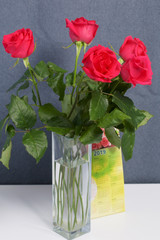 A bouquet of scarlet roses in a glass vase. Next is a calendar. On a gray background.