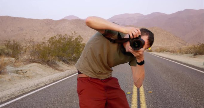 Young trendy male photographer in desert bending over taking photo
