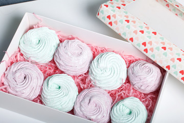 Homemade marshmallows of different colors are beautifully packed in a gift box. Nearby is the lid of the box with a transparent window. On a white background.
