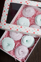 Homemade marshmallows of different colors are beautifully packed in a gift box. Nearby is the lid of the box with a transparent window. On a dark background.