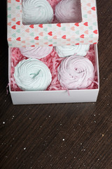 Homemade marshmallows of different colors are beautifully packed in a gift box. Nearby is the lid of the box with a transparent window. On a dark background.