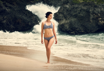 A girl in a swimsuit is walking along the beach. Ocean coast. Bali. Bingin Beach. Asia. Journey. Rocks on the beach.