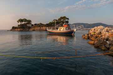 An old fishing ship anchored in the port of Zakynthos (Gretsai) on the background of a picturesque beach in the rays of the setting sun.