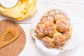 Cottage cheese cookies sprinkled with sugar in a basket and a cup of milk on a wooden table. Top view