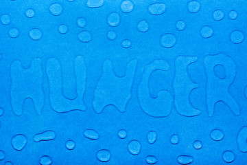 The word "hunger" is written with water droplets and water droplets on a blue smooth surface. Top view