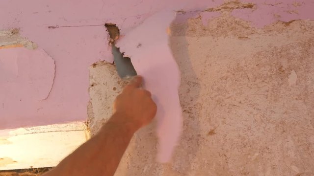 Decrepit pink wallpaper on the wall, home repair. Man peeling old wallpaper with special spatula.