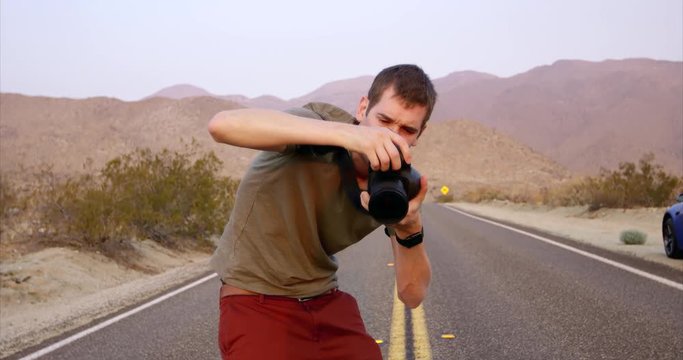 Young trendy male photographer reviewing photos on camera - desert in the background