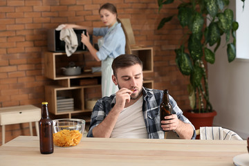 Lazy husband drinking beer while his wife doing chores