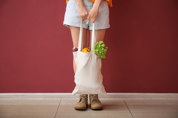 Young woman with vegetables in eco bag near color wall