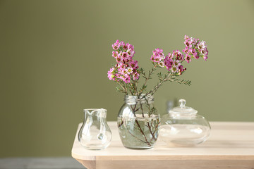 Jar with beautiful flowers on table against color background