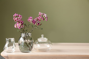 Jar with beautiful flowers on table against color background