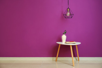 Table with vase and new lamp hanging on color wall