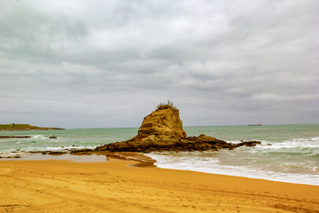Rock in the middle ofthe beach with warm tones and a cloudy sky