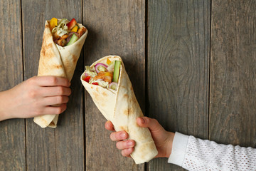 Female hands with tasty doner kebab on wooden background - obrazy, fototapety, plakaty