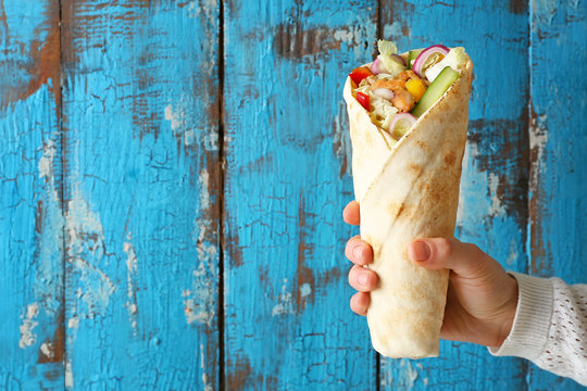 Female hand with tasty doner kebab on color wooden background
