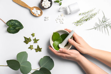 Female hands with mortar, different herbs and plant based pills on white background