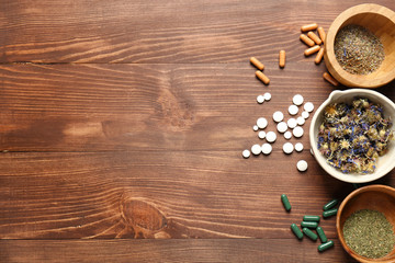 Composition with plant based pills and herbs on wooden background