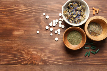 Composition with plant based pills and herbs on wooden background