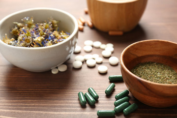 Plant based pills and bowls with dry herbs on wooden background