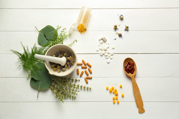 Fototapeta na wymiar Composition with mortar, herbs and plant based pills on white wooden background
