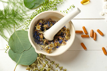 Mortar with dry flowers, herbs and plant based pills on table © Pixel-Shot