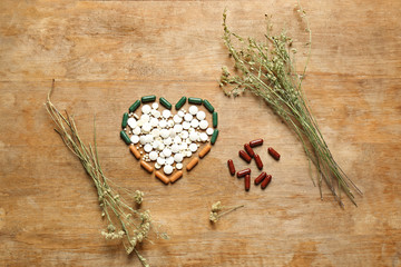 Heart made of plant based pills on wooden background