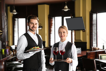 Young waiters with wine and salad in restaurant