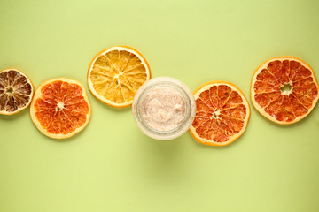 Jar of sugar scrub with citrus slices on color background