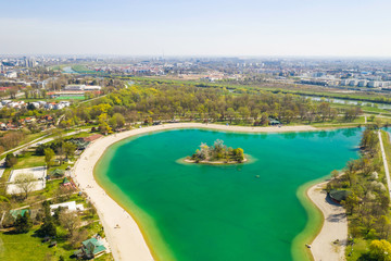Fototapeta premium Zagreb, Croatia, Jarun lake, beautiful green recreation park area, sunny spring day, panoramic view from drone, city in background