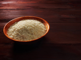 White basmati rice in a bamboo bowl on a brown wooden background