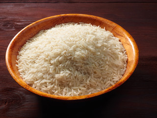 White basmati rice in a bamboo bowl on a brown wooden background