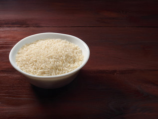 White basmati rice in a white bowl on a brown wooden background