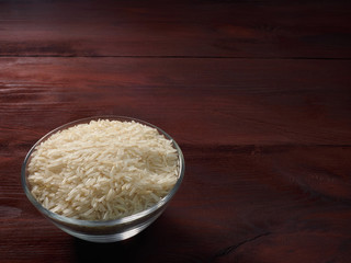 White basmati rice in a glass bowl on a brown wooden background