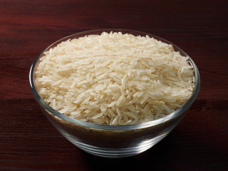White basmati rice in a glass bowl on a brown wooden background