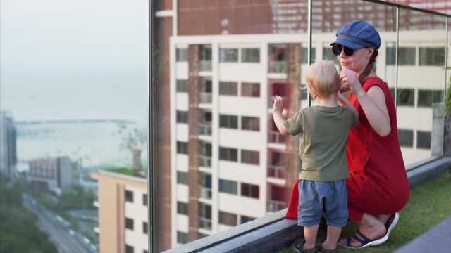 A two-year-old child and his mother stand on the observation deck and look to the urban landscape. Pattaya, Thailand.