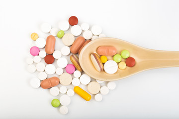 Colorful medical pills on spoon and capsules or supplements for therapy in background, concept of treatment and health care