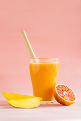 Mango and orange smoothie in glass on pink background.