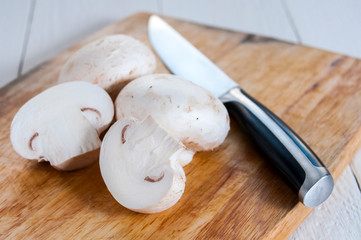 Fresh champignons and a knife on a wooden cutting board.