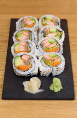 salmon, avocado and carrot sushi roll served on a slate plate with ginger and wasabi