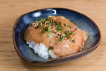 bowl with salmon sashimi seasoned with black and white sesame, rocket, nori seaweed fried on a bed of steamed white rice
