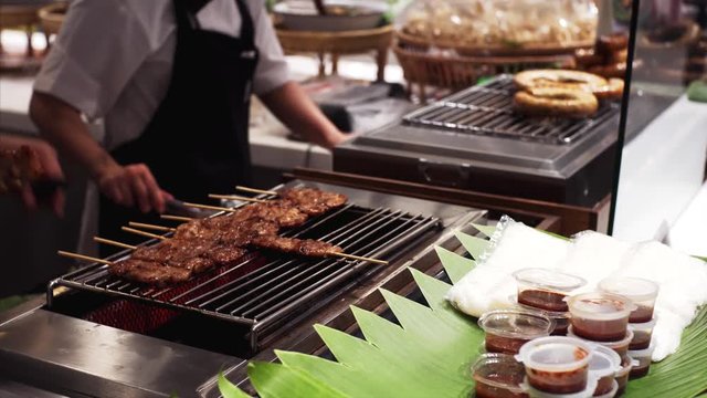 Unidentified chiefs are preparing grilled meat in thai food court