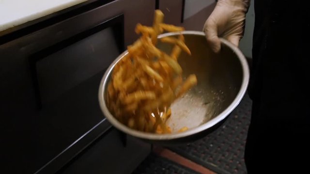 chef flipping flip tosses beer battered fries in metal bowl slow motion.  A chef flips a bowl full of french fries to evenly mix the seasonings.
