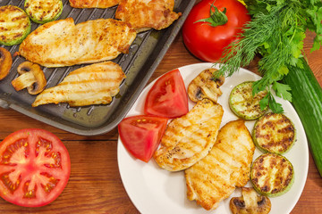Grilled chicken meat on dish and grill pan, vegetables, greens