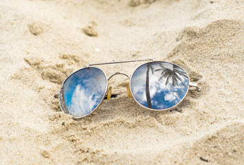 Fototapeta na wymiar Mirrored sunglasses close up on the beach sand with palm trees reflection