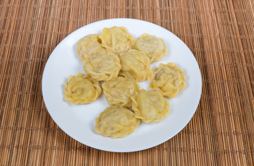 Cooked homemade meat dumplings on dish on bamboo table mat