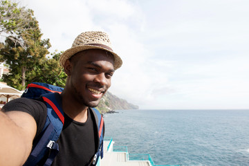 happy young black travel man smiling while taking selfie by the sea