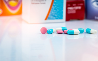 Round pink tablets pill and white-blue capsule pills on blurred background of drug packaging....