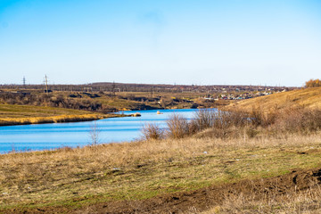 Early spring landscape, in the Rostov region in the city of Shakhty, on the Grushevka river. Sunny sunset in yellow and orange warm light. Dry grass on the local shore and a beautiful reflection in th