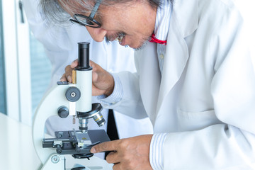 Senior male supervisor scientist looking through a microscope in a laboratory. Health care researchers working in life science laboratory.