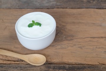 Natural homemade plain organic yogurt in white bowl and wood spoon on wood texture background